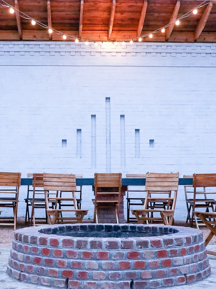 The fire-pit gathering courtyard at The Bend at Carlton Landing — wooden chairs around a long communal table with string lights overhead