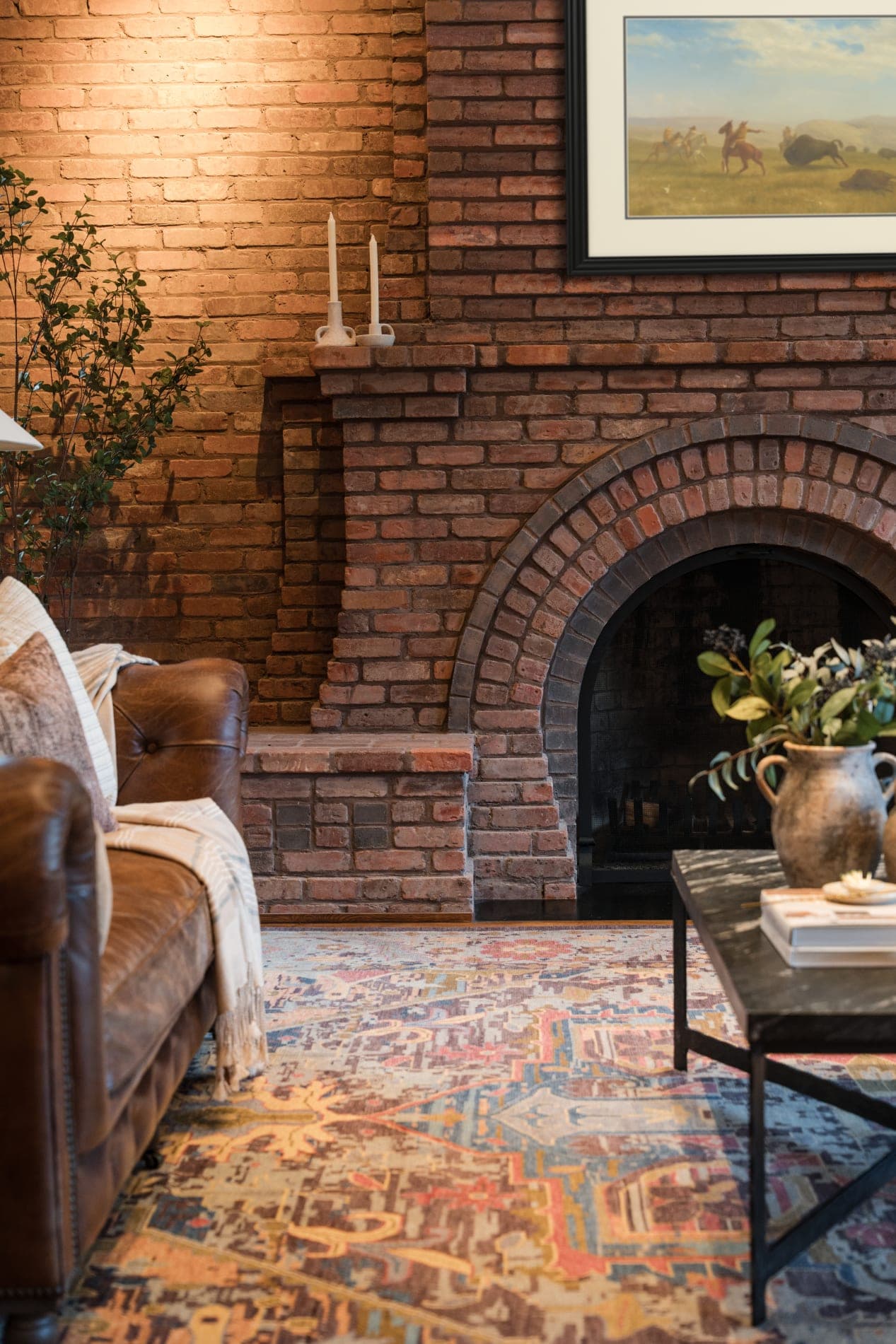 Living room interior with a brick arched fireplace, leather chesterfield sofa, vintage Persian rug, and a period plains-painting on the brick
