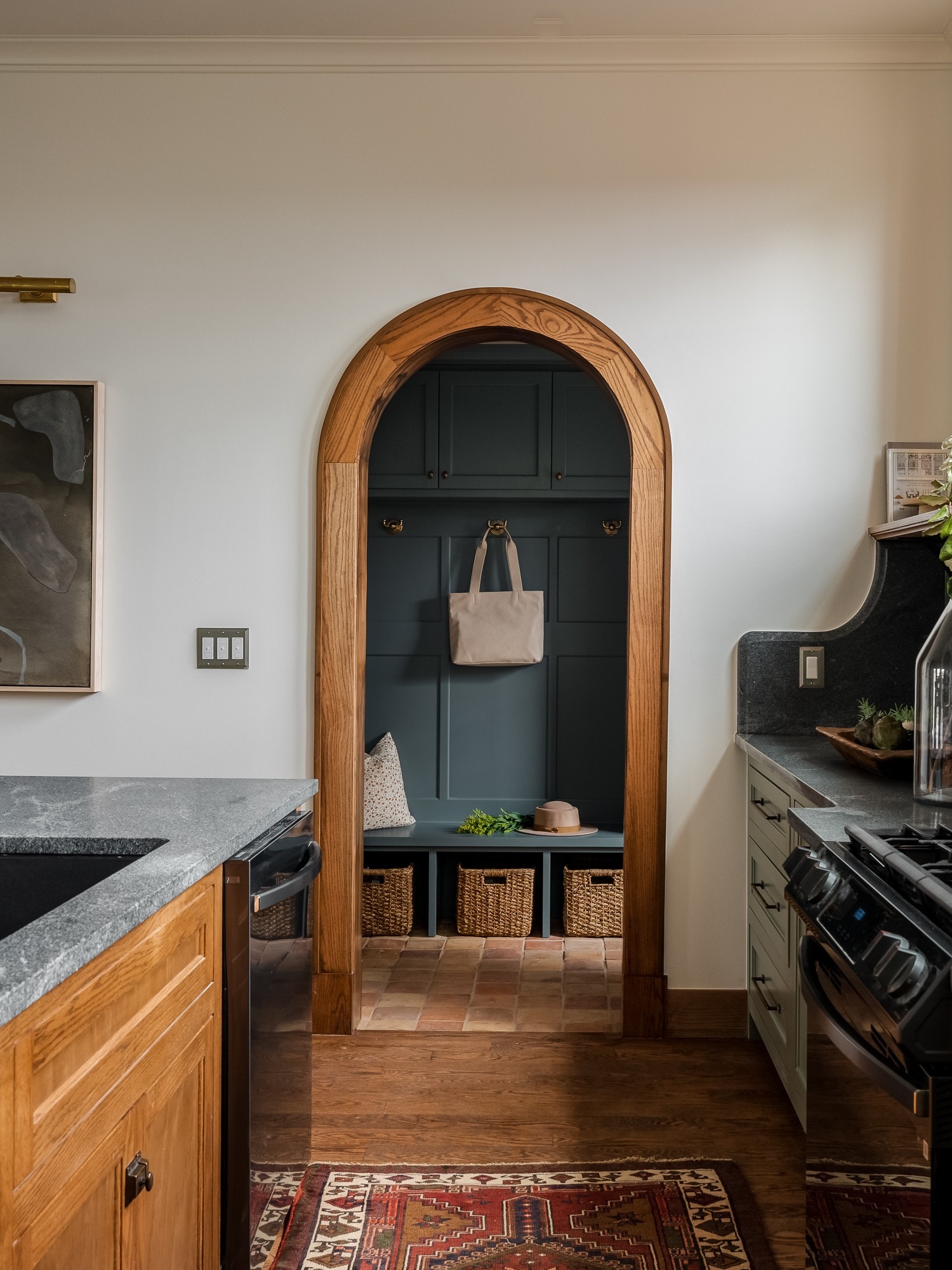 Kitchen interior with an oak-trimmed arched mudroom doorway, soapstone counters, olive cabinets, and period architectural detailing