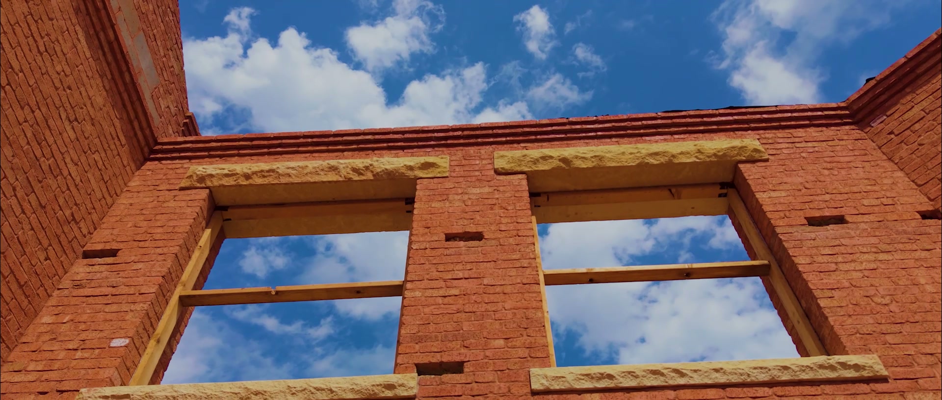 Structural brick walls with cut-stone lintels rising against an Oklahoma sky at a Building Culture project under construction.